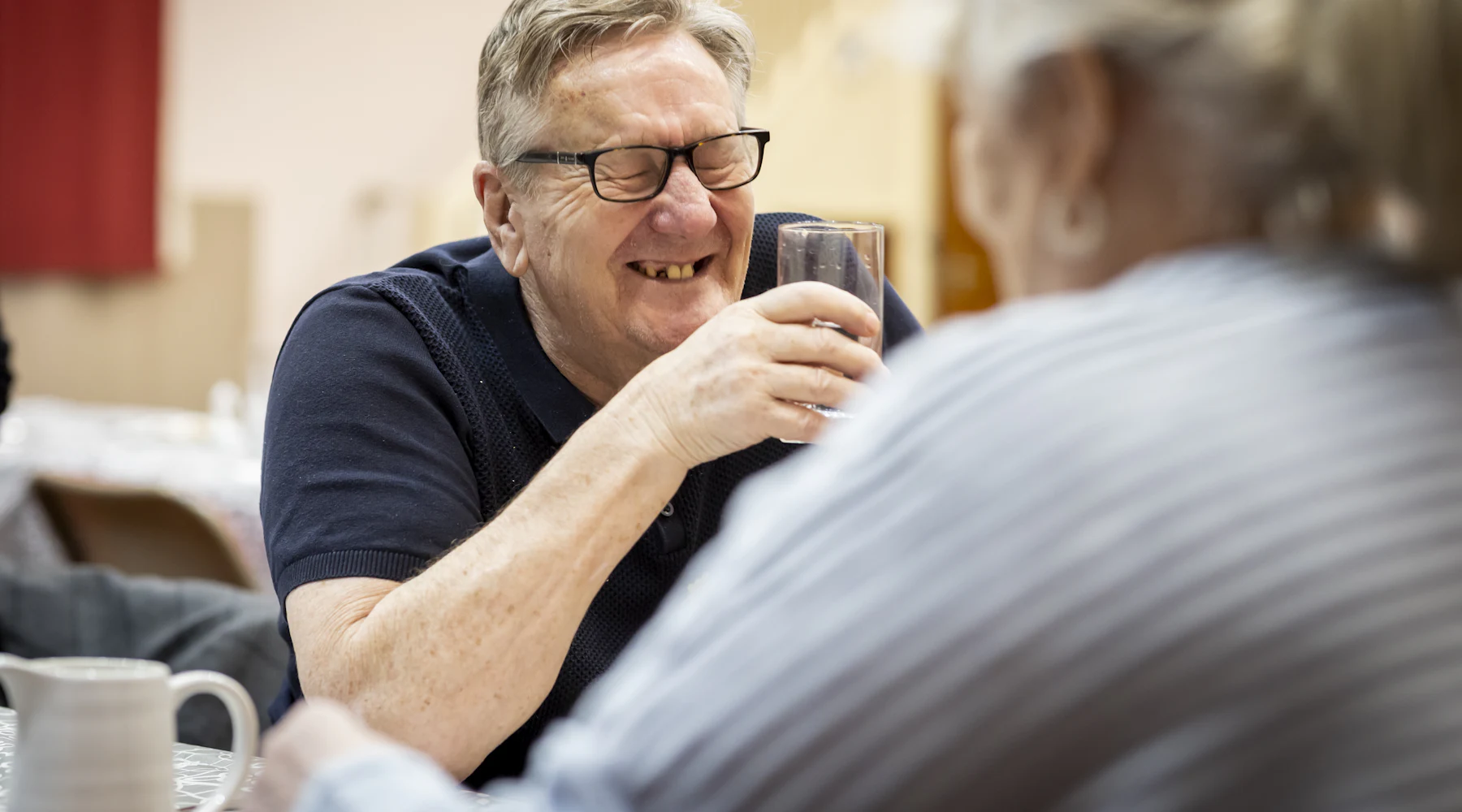 Un homme âgé qui rit, un verre à la main, entouré